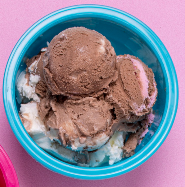 Bol de helado con bolas de chocolate y vainilla, presentado sobre una superficie rosa.